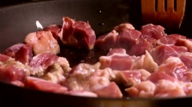 Et parçaları tavada kızartılır. Mutfakta öğle yemeği pişir. Ahşap mutfak spatulasıyla karıştır..