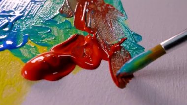 Resim tuvalinde çok renkli boyalar var. Yağlı boyaları fırçayla karıştır. Sarı mavi kırmızı.