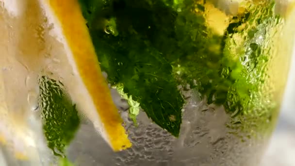 Refrescante refresco con hielo. Mojito con limón y menta en un vaso. Agua carbonatada de cerca. Gotas de rocío frío en un vaso. — Vídeo de stock