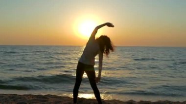 Şafakta deniz kenarında sabah egzersizi yapan bir kız. Okyanusun arka planında egzersiz yap. Açık hava fitness dersleri. Günün etkin başlangıcı.