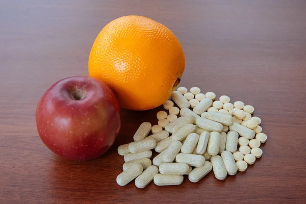 Manzana roja, naranja y pastillas en la mesa —  Fotos de Stock