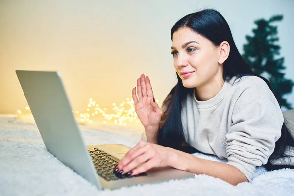 Beautiful girl celebrate with laptop, success happy pose. Smiling hipster girl talking and waving hand hello during online video call via laptop computer, sitting at home.