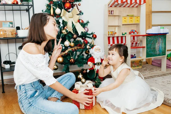 クリスマスツリーの近くに座って贈り物を持つ2人の姉妹 ロイヤリティフリーのストック写真