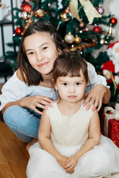 クリスマスツリーの近くに座って贈り物を持つ2人の姉妹 ロイヤリティフリーのストック写真