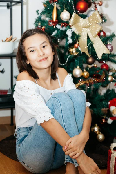 漂亮的12岁少女坐在圣诞树下 带着圣诞礼物 坐在房间的地板上 图库图片