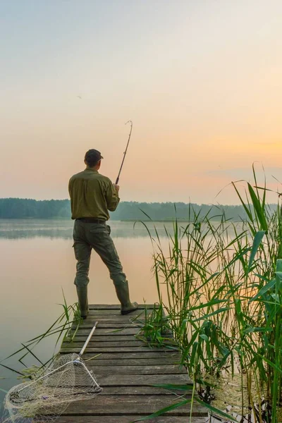 木の桟橋から夜明けに魚を捕まえる釣り人 — ストック写真
