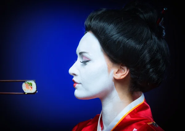 Женщина в гриме гейши ест суши — стоковое фото