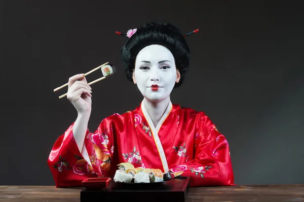 Kvinna i geisha makeup äta sushi Stockfoto