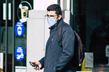 Fransa 'yı 16 Şubat 2021' de Reims sokaklarında yürüyen ve Fransa 'yı etkileyen salgın sırasında kendilerini koronavirüsten korumak için maske takan kimliği belirsiz bir yaya.