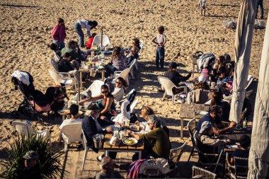 Tel Aviv, İsrail, 13 Ocak 2026 Akdeniz kıyısındaki bir restoranda oturan insanlar. Kumsal, dalgalar ve deniz kenarındaki gezinti, İsrail kıyılarının doğal güzelliğinin olağanüstü bir manzarası..