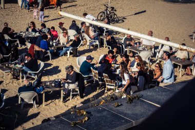 Tel Aviv, İsrail, 13 Ocak 2026 Akdeniz kıyısındaki bir restoranda oturan insanlar. Kumsal, dalgalar ve deniz kenarındaki gezinti, İsrail kıyılarının doğal güzelliğinin olağanüstü bir manzarası..