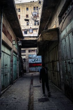 Hebron, Filistin Bölgesi, 31 Ocak 2026 Dikey Ayrımcılık. Üst katlardaki İsrailli göçmen çocuklar Filistin sokaklarına bakıyor. Metal ağ pazarı fırlatılan nesnelerden korur.