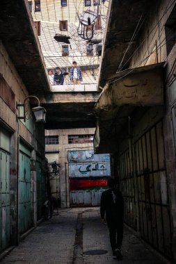 Hebron, Filistin Bölgesi, 31 Ocak 2026 Dikey Ayrımcılık. Üst katlardaki İsrailli göçmen çocuklar Filistin sokaklarına bakıyor. Metal ağ pazarı fırlatılan nesnelerden korur.