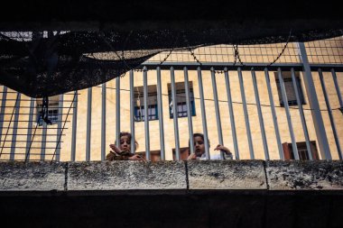 Hebron, Filistin Bölgesi, 31 Ocak 2026 Dikey Ayrımcılık. Üst katlardaki İsrailli göçmen çocuklar Filistin sokaklarına bakıyor. Metal ağ pazarı fırlatılan nesnelerden korur.