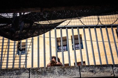 Hebron, Filistin Bölgesi, 31 Ocak 2026 Dikey Ayrımcılık. Üst katlardaki İsrailli göçmen çocuklar Filistin sokaklarına bakıyor. Metal ağ pazarı fırlatılan nesnelerden korur.