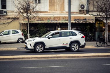 Tel Aviv, İsrail - 23 Şubat 2026: Şehir merkezinde yoğun bir kavşaktan geçen beyaz bir taksi. Şehir trafiği hafta içi Akdeniz Hitech metropolünün yüksek yoğunluk ve ekonomik faaliyetlerini yansıtıyor.