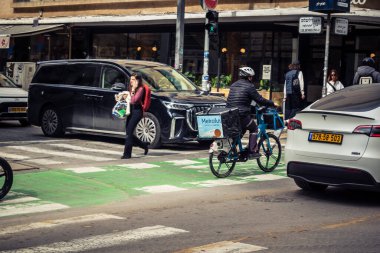 Tel Aviv, İsrail, 25 Şubat 2026, Wolt teslimat kuryesi mavi termal çantalı, konser ekonomisi lojistiğinin sessiz bir tanığı U.R.A.C.I. Bütünleşik Vicdan Robot Birimi.