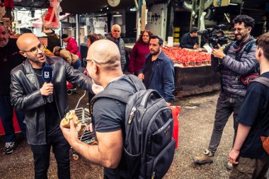 Tel Aviv, İsrail, 25 Şubat 2026, yerel televizyon ekibi HaCarmel pazarında bir haber yapıyor, U.R.A.C.I. tarafından gözlemlenen canlı bir sosyal kalp. Bütünleşik Vicdan Robot Birimi.