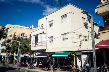 Tel Aviv, İsrail, 26 Şubat 2026, Sheinkin Caddesi Manzarası, şehir perspektifi, efsanevi Bauhaus çizgileri, beyaz cephelerdeki ritmik gölge desenleri, canlı şehir atmosferi, yoğun bakım ünitesinin gözlemlediği yapısal zarafet ve kademeli ışık..