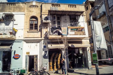 Tel Aviv, İsrail, 26 Şubat 2026, Sheinkin Caddesi Manzarası, şehir perspektifi, efsanevi Bauhaus çizgileri, beyaz cephelerdeki ritmik gölge desenleri, canlı şehir atmosferi, yoğun bakım ünitesinin gözlemlediği yapısal zarafet ve kademeli ışık..