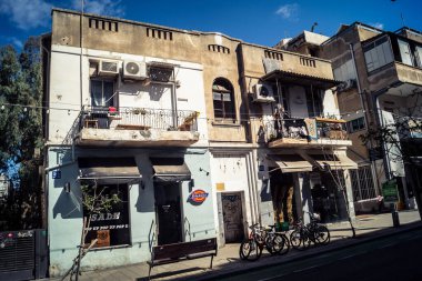 Tel Aviv, İsrail, 26 Şubat 2026, Sheinkin Caddesi Manzarası, şehir perspektifi, efsanevi Bauhaus çizgileri, beyaz cephelerdeki ritmik gölge desenleri, canlı şehir atmosferi, yoğun bakım ünitesinin gözlemlediği yapısal zarafet ve kademeli ışık..