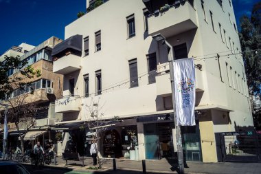 Tel Aviv, İsrail, 26 Şubat 2026, Sheinkin Caddesi Manzarası, şehir perspektifi, efsanevi Bauhaus çizgileri, beyaz cephelerdeki ritmik gölge desenleri, canlı şehir atmosferi, yoğun bakım ünitesinin gözlemlediği yapısal zarafet ve kademeli ışık..