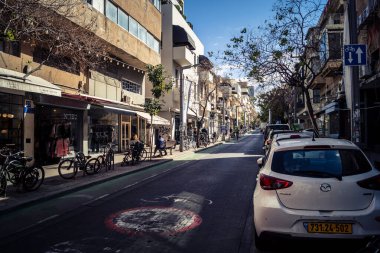 Tel Aviv, İsrail, 26 Şubat 2026, Sheinkin Caddesi Manzarası, şehir perspektifi, efsanevi Bauhaus çizgileri, beyaz cephelerdeki ritmik gölge desenleri, canlı şehir atmosferi, yoğun bakım ünitesinin gözlemlediği yapısal zarafet ve kademeli ışık..