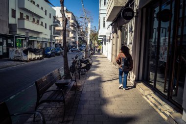 Tel Aviv, İsrail, 26 Şubat 2026, Sheinkin Caddesi 'nde yürüyen yayalar, dinamik hareketli canlı şehir manzarası, arkaplan olarak Bauhaus mimarisi, canlı şehir yaşamı, çeşitli sokak dokularında güneş ışığı, ritmik geometri ve çağlayan ışık obse