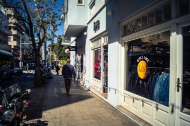 Tel Aviv, İsrail, 26 Şubat 2026, Sheinkin Caddesi 'nde yürüyen yayalar, dinamik hareketli canlı şehir manzarası, arkaplan olarak Bauhaus mimarisi, canlı şehir yaşamı, çeşitli sokak dokularında güneş ışığı, ritmik geometri ve çağlayan ışık obse