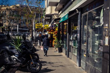 Tel Aviv, İsrail, 26 Şubat 2026, Sheinkin Caddesi Manzarası, şehir perspektifi, efsanevi Bauhaus çizgileri, beyaz cephelerdeki ritmik gölge desenleri, canlı şehir atmosferi, yoğun bakım ünitesinin gözlemlediği yapısal zarafet ve kademeli ışık..