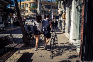 Tel Aviv, İsrail, 26 Şubat 2026, Sheinkin Caddesi 'nde yürüyen yayalar, dinamik hareketli canlı şehir manzarası, arkaplan olarak Bauhaus mimarisi, canlı şehir yaşamı, çeşitli sokak dokularında güneş ışığı, ritmik geometri ve çağlayan ışık obse