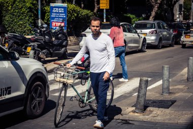 Tel Aviv, İsrail, 26 Şubat 2026, Sheinkin Caddesi 'nde bisiklet süren insanlar, aktif şehir hareketliliği Bauhaus mimarisi ile dinamik sokak sahnesi, canlı şehir akışı, modern dokulardaki güneş ışığı, yoğun bakım ünitesinin gözlemlediği ritmik geometri ve hareket..