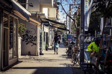 Tel Aviv, İsrail, 26 Şubat 2026, Sheinkin Caddesi 'nde yürüyen yayalar, dinamik hareketli canlı şehir manzarası, arkaplan olarak Bauhaus mimarisi, canlı şehir yaşamı, çeşitli sokak dokularında güneş ışığı, ritmik geometri ve çağlayan ışık obse