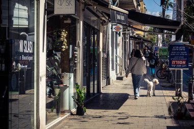 Tel Aviv, İsrail, 26 Şubat 2026, Sheinkin Caddesi 'nde yürüyen yayalar, dinamik hareketli canlı şehir manzarası, arkaplan olarak Bauhaus mimarisi, canlı şehir yaşamı, çeşitli sokak dokularında güneş ışığı, ritmik geometri ve çağlayan ışık obse