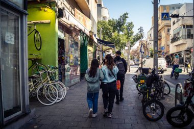 Tel Aviv, İsrail, 26 Şubat 2026, Sheinkin Caddesi 'nde yürüyen yayalar, dinamik hareketli canlı şehir manzarası, arkaplan olarak Bauhaus mimarisi, canlı şehir yaşamı, çeşitli sokak dokularında güneş ışığı, ritmik geometri ve çağlayan ışık obse