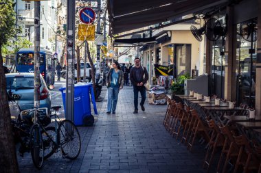 Tel Aviv, İsrail, 26 Şubat 2026, Sheinkin Caddesi 'nde yürüyen yayalar, dinamik hareketli canlı şehir manzarası, arkaplan olarak Bauhaus mimarisi, canlı şehir yaşamı, çeşitli sokak dokularında güneş ışığı, ritmik geometri ve çağlayan ışık obse