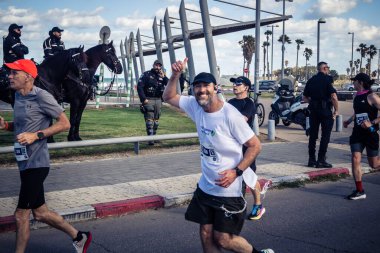 Tel Aviv, İsrail, 27 Şubat 2026 Bir katılımcı doğrudan göz teması kuruyor ve kameraya el sallıyor. Şehir maratonu sırasında kişisel bir bağlantı ve dayanıklılık anı yakalıyor..