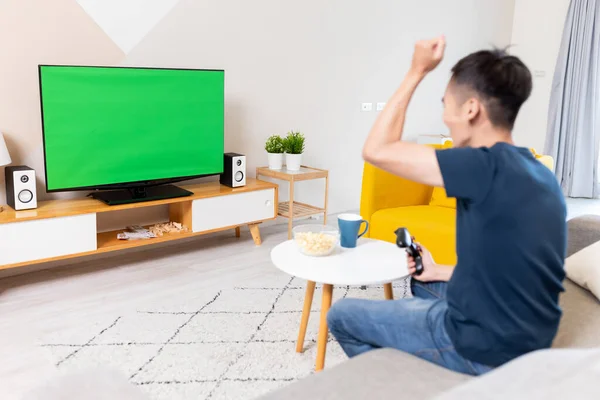 亚洲年轻的游戏玩家男孩坐在沙发上 手里拿着无线控制器 在家里的绿色彩色关键电视屏幕上玩电子游戏 赢得了比赛 — 图库照片