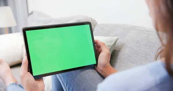 Person use tablet pc with green screen lying on sofa in the living room