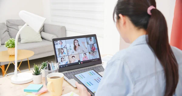 亚洲女性员工的后视镜可以在家里通过笔记本电脑与同事进行视频会面 并使用平板电脑查看她的数据 — 图库照片