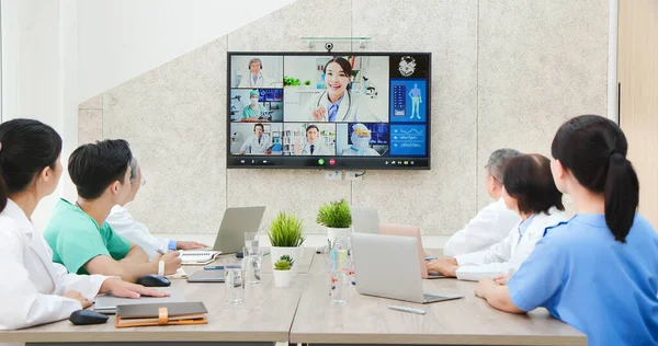 asian young female doctor chatting to medical team using online video chat on tv screen discussing about their thoughts and studies