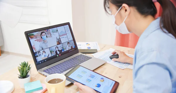 持面部面具的亚裔女性员工在家里用笔记本电脑与同事们进行视频会面 — 图库照片