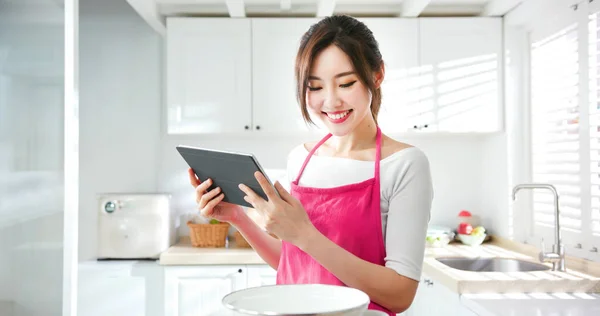 亚洲漂亮的家庭主妇用平板电脑在网上寻找烹调秘诀 — 图库照片
