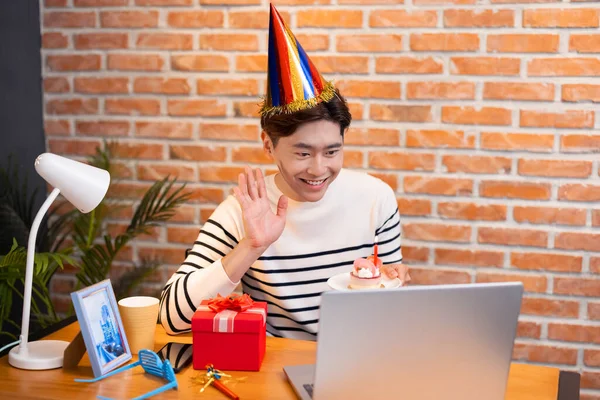 모자를 아시아인 청년은 친구를 케이크를 축하하고 주면서 노트북으로 비디오 채팅을 — 스톡 사진