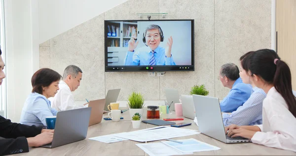 一群亚洲商人在会议室开电话会议 一位年事已高的领导人通过电视屏幕上的在线视频聊天和同事们聊天 讨论办公室里的想法 — 图库照片