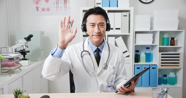 아시아인 의사는 웹캠으로 환자와 대화하고 디지털 태블릿에 필기를 헤드셋을 — 스톡 사진