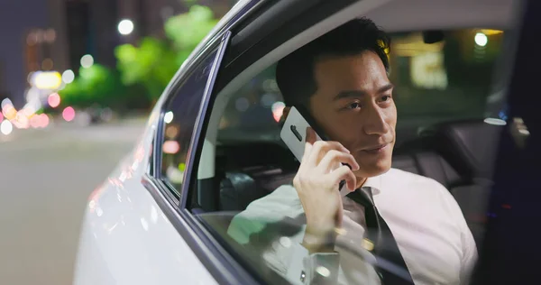 亚洲商人在夜间乘出租车通勤时用智能手机交谈 — 图库照片