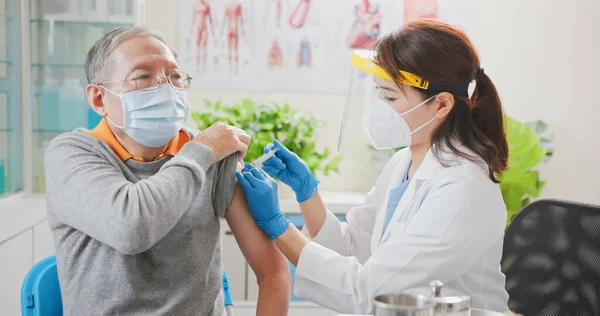 亚洲女医生戴着手套和隔离面具 在医院的老年男性病人肩部接种了Covid 19疫苗 — 图库照片