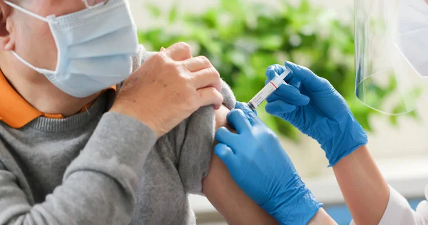 一名戴着手套和隔离面具的亚洲女医生正在医院的老年男性患者肩部接种Covid 19疫苗 — 图库照片