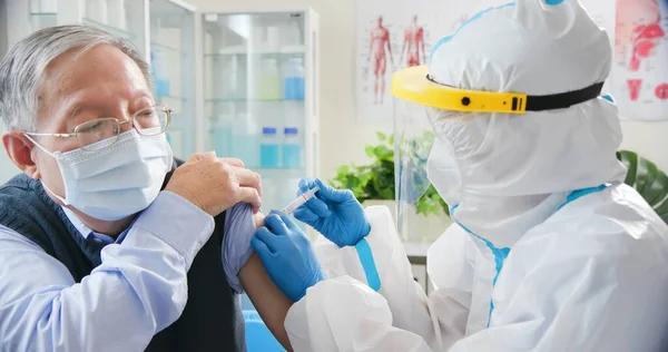 亚洲女护士身穿手套和隔离衣 在医院的老年男病人肩部接种了Covid 19疫苗 — 图库照片